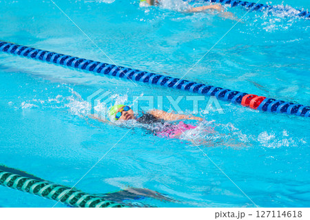Swimmer child swims backstroke swimming style in a race swimming pool. Water sports and competition, learning to swim classes for children. Swimmer child swims backstroke swimming style in a race swimming pool. Water sports and competition, learning to swim classes for children. 127114618