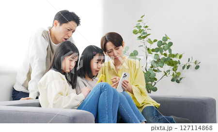 スマホを見ながら困った表情の小学生の女の子の家族 127114868