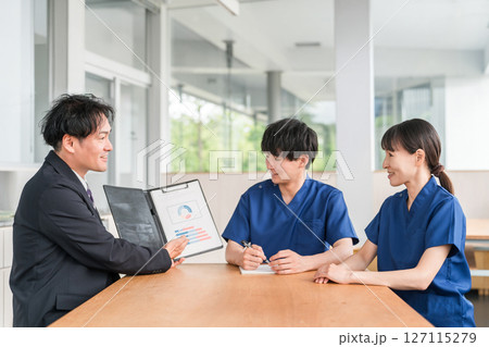 営業,商談する医療機器メーカーの男性ビジネスマンとスクラブ姿の医療従事者の男女 127115279