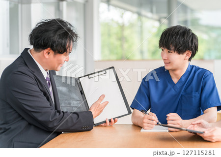 営業,商談する医療機器メーカーの男性ビジネスマンとスクラブ姿の医療従事者の男女 営業,商談する医療機器メーカーの男性ビジネスマンとスクラブ姿の医療従事者の男女 127115281