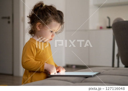 Young girl focused on digital drawing on a tablet. Cozy family space in the background. Young girl focused on digital drawing on a tablet. Cozy family space in the background. 127116048