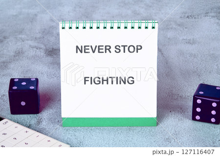 The concept of inspirational and motivational. NEVER STOP FIGHTING written on a desktop notebook, surrounded by a calculator and dice 127116407