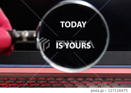 Motivational words TODAY IS YOURS through a magnifying glass on a laptop screen in a dimly lit room 127116475
