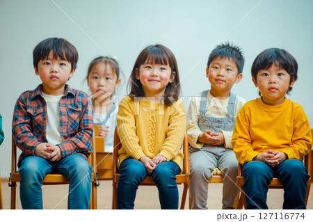 A group of children sitting on wooden chairs in a row A group of children sitting on wooden chairs in a row 127116774