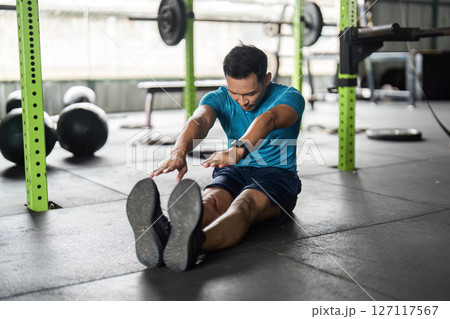Fitness Stretching Exercise. Young man reaching for his toes on the gym floor. 127117567