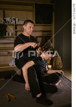 Male master giving Thai Toksen massage to girl in massage room. A girl gets a relaxing Thai back massage with a Toxen massage kit Male master giving Thai Toksen massage to girl in massage room. A girl gets a relaxing Thai back massage with a Toxen massage kit 127118270