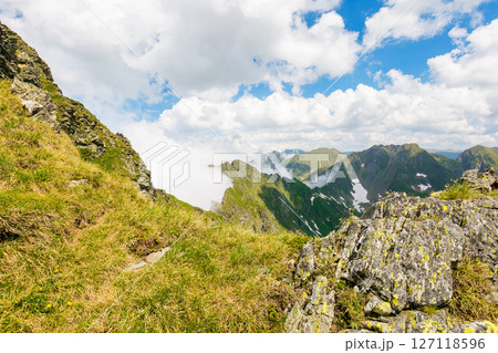 alpine landscape of romania in summer. rocky scenery. fagaras mountain ridge on a sunny day. scenic valley with snow on the grassy slope beneath a blue sky with clouds. travel to transylvania alpine landscape of romania in summer. rocky scenery. fagaras mountain ridge on a sunny day. scenic valley with snow on the grassy slope beneath a blue sky with clouds. travel to transylvania 127118596