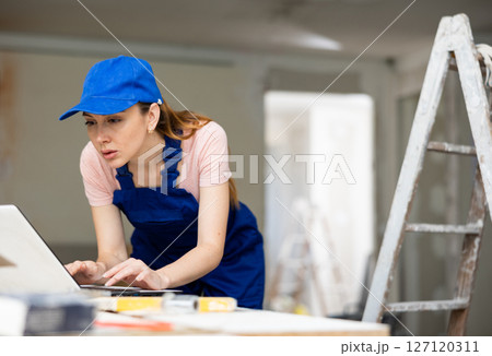 Portrait of a female builder who checks the work done using laptop 127120311