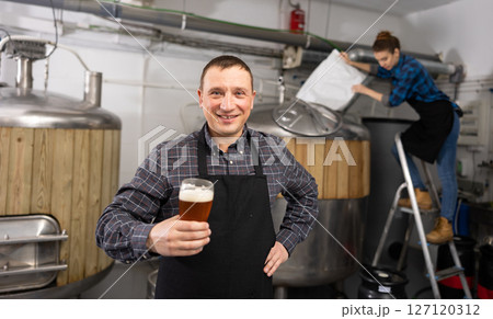 Satisfied professional brewer holding out glass with craft beer 127120312