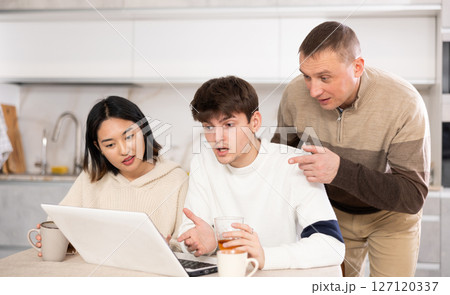 Friendly family watches something together on the Internet or video chats via laptop Friendly family watches something together on the Internet or video chats via laptop 127120337