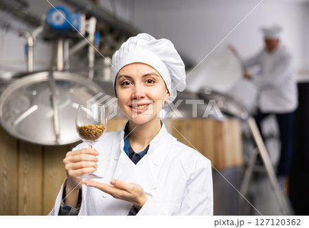 Portrait of positive female brewer with a glass of barley at brewery 127120362