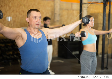 Focused man pumping up deltoid muscles with dumbbells in gym 127120440