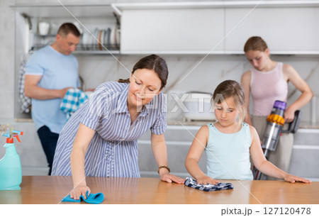 Little girl helps mother wash kitchen table. 127120478
