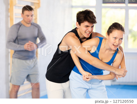Self-defense class - a woman learns to fight back an attacking man under the guidance of trainer Self-defense class - a woman learns to fight back an attacking man under the guidance of trainer 127120550