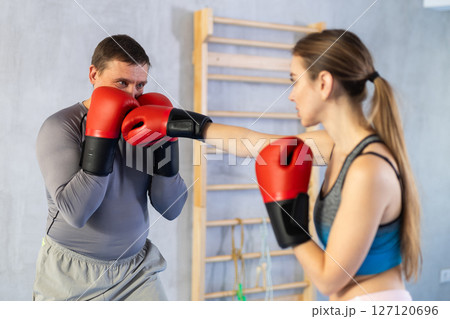 Woman and man in sportswear are engaged in boxing sparring in gym Woman and man in sportswear are engaged in boxing sparring in gym 127120696