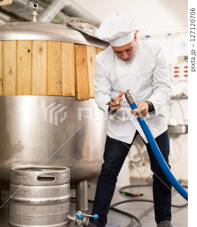 Brewer connects a hose to barrel of beer 127120706