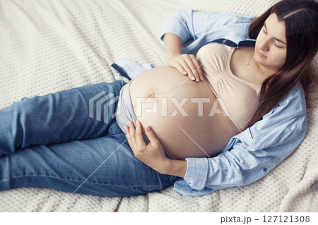 A pregnant woman is seen resting comfortably on bed. She appears content and serene, enjoying a quiet moment 127121308