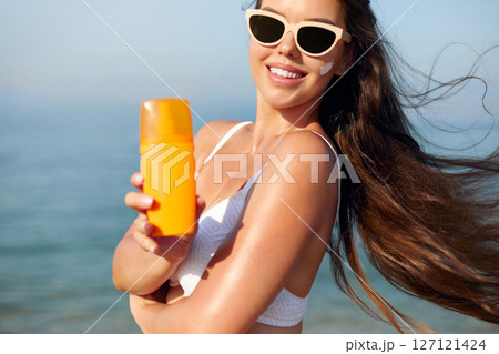 Beautiful Woman in Bikini Applying Sun Cream on Tanned Shoulder. Sun Protection. Skin and Body Care. Girl Using Sunscreen.  Portrait Of Female Holding Suntan Lotion or Moisturizing Sunblock. 127121424