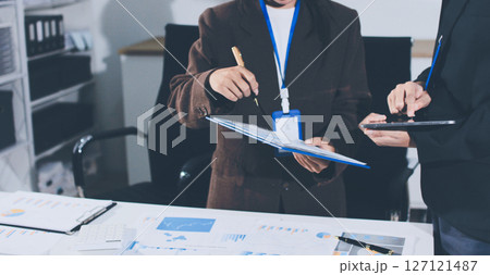 Focused young businessman signing agreement with skilled lawyer in eyeglasses. Concentrated financial advisor showing place for signature on paper contract document to male client at meeting in office 127121487