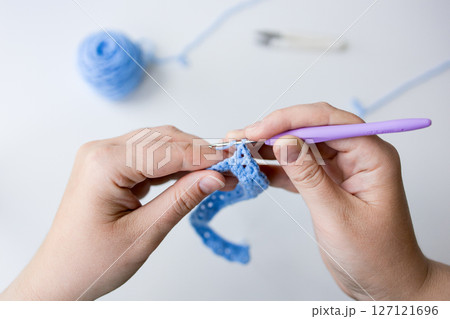Close up of crocheting hands with purple hook and blue yarn Close up of crocheting hands with purple hook and blue yarn 127121696