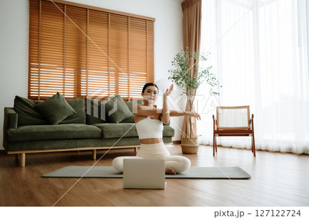 Happy young Asian woman practicing yoga and shoulder stretching at home Happy young Asian woman practicing yoga and shoulder stretching at home 127122724