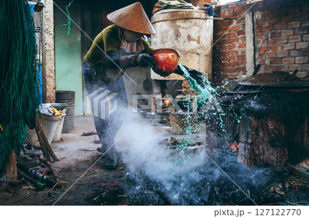 Vietnamese female worker puts out a fire in furnace in a reed dyeing workshop at factory in a village. Asian woman does dirty hard men's work in a factory in Asia 127122770