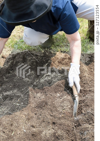 肥料をまいた家庭菜園の土をシャベルで均しているシニア女性 肥料をまいた家庭菜園の土をシャベルで均しているシニア女性 127123554