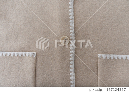 Minimal close-up of wool blend coat with decorative stitch and single button on beige fabric 127124537