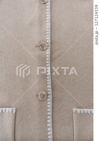 Wool blend coat detail with buttons and decorative white trim on beige fabric Wool blend coat detail with buttons and decorative white trim on beige fabric 127124539