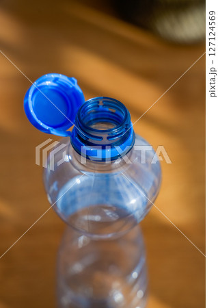 Open plastic bottle with attached blue cap on wooden background in sunlight Open plastic bottle with attached blue cap on wooden background in sunlight 127124569