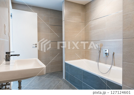 Minimalist bathroom interior with a white bathtub, wall-mounted sink, and chrome faucet.  127124601