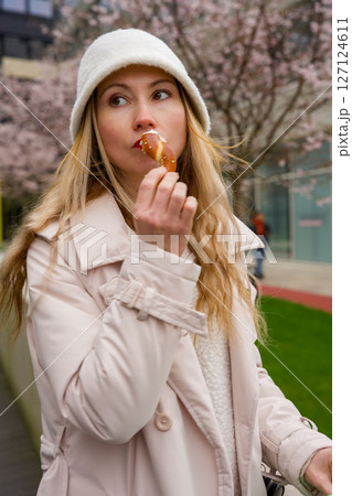 Modern elegance: Woman enjoying pretzel in Prague city park. Modern elegance: Woman enjoying pretzel in Prague city park. 127124611
