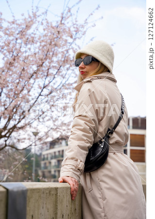 Elegant woman in a white bucket hat enjoying springtime under cherry blossoms in a modern cityscape 127124662