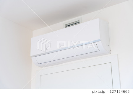 Modern white wall-mounted air conditioner unit in a home interior 127124663