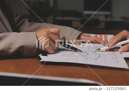 Group of confident business people point to graphs and charts to analyze market data, balance sheet, account, net profit to plan new sales strategies to increase production capacity. 127125063