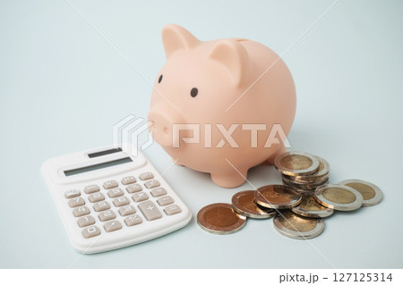 Close up pink piggy bank on light blue background overflowing coins and calculator. 127125314