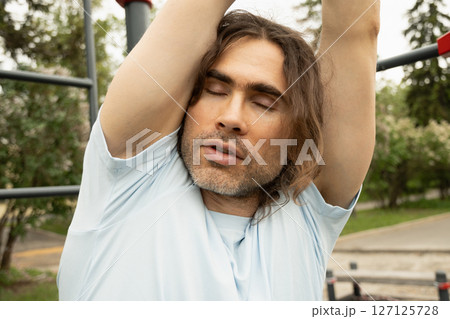 Athlete is tired of doing exercises and wants. Funny hanging on horizontal bar at sports ground. Impact of bad weather. Close up. 127125728