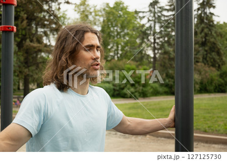 Portrait of tired sporty caucasian man thoughtful expression, lost in thought at public park near sport ground equipment. Laziness, forces himself to exercise. Slow living. Outdoor 127125730