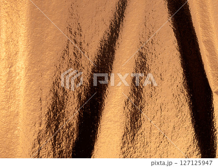 Golden and bronze foil texture with a glossy, shiny finish, creating a sleek, luxurious backdrop. 127125947
