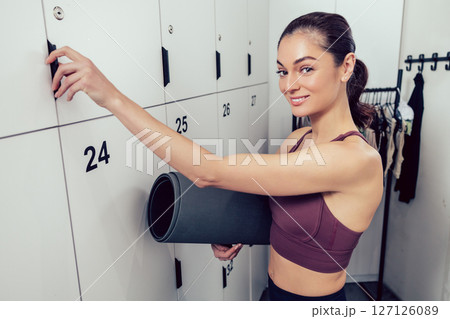 Smiling young woman with a rolled mat opening a locker in the gym Smiling young woman with a rolled mat opening a locker in the gym 127126089