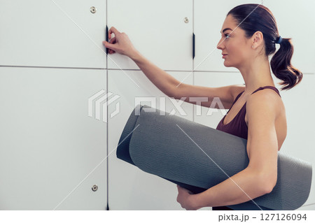 Dark-haired young woman opening locker in the locker room in the gym Dark-haired young woman opening locker in the locker room in the gym 127126094