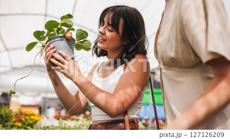 Woman choosing strawberry plant in greenhouse with friend Woman choosing strawberry plant in greenhouse with friend 127126209