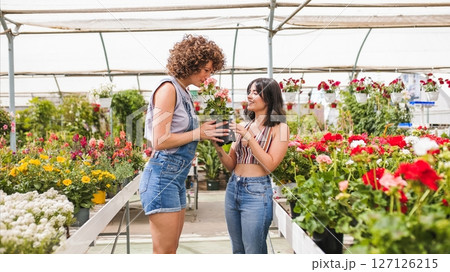 Young women smelling blooming flowers inside greenhouse nursery Young women smelling blooming flowers inside greenhouse nursery 127126215