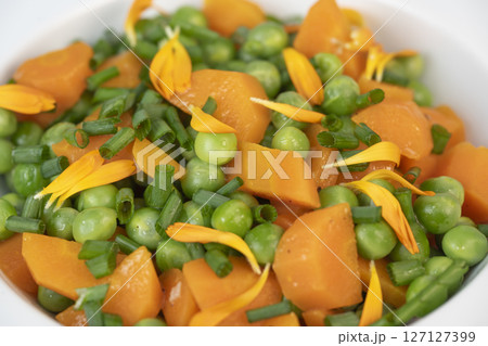 Fresh garden peas and carrots cooked in butter, garnished with chives and marigold flowers for a 127127399