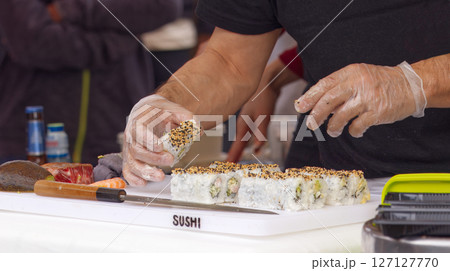 Chef Preparing Fresh Sushi Rolls on White Cutting Board 127127770