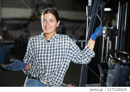 Young woman posing by forklift in workshop 127128020