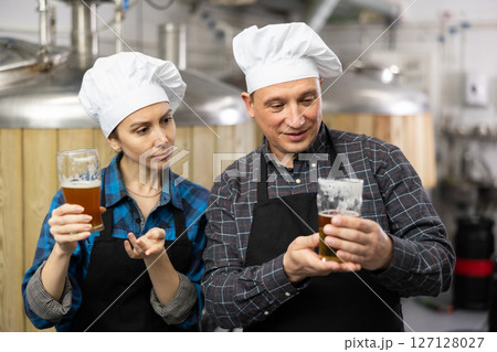 Brewers man and woman is standing with glasses for beer on workplace indoor Brewers man and woman is standing with glasses for beer on workplace indoor 127128027