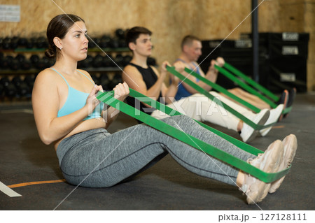 Focused young woman training with resistance band for health wellness, strong biceps or abs muscles in gym health center Focused young woman training with resistance band for health wellness, strong biceps or abs muscles in gym health center 127128111