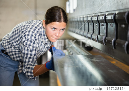 Young woman bends sheet of metal under pressure Young woman bends sheet of metal under pressure 127128124
