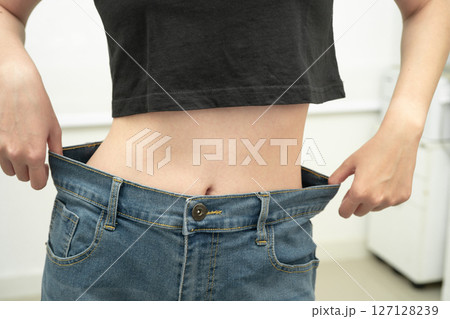 Young Asian woman losing weight wearing loose pants in oversize jeans. Young Asian woman losing weight wearing loose pants in oversize jeans. 127128239